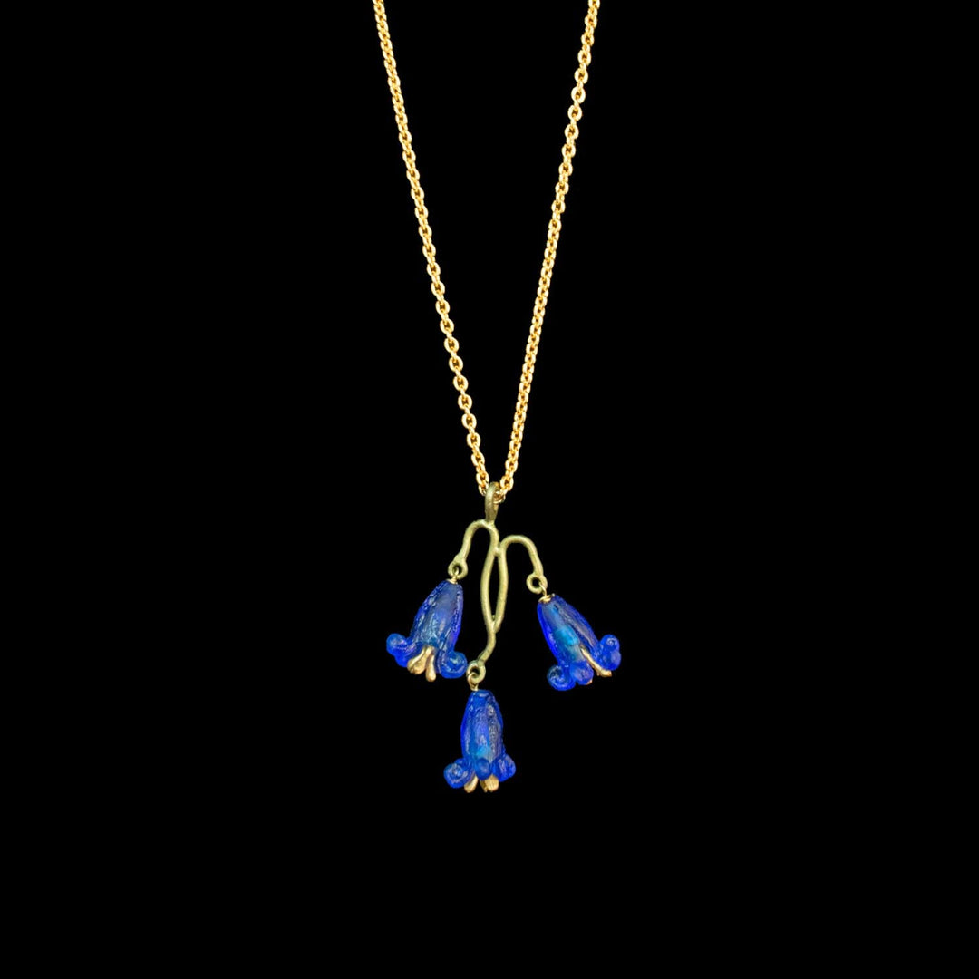 A gold chain necklace featuring three dangling bell-shaped blue flowers with gold-toned outlines, shown against a solid black background.