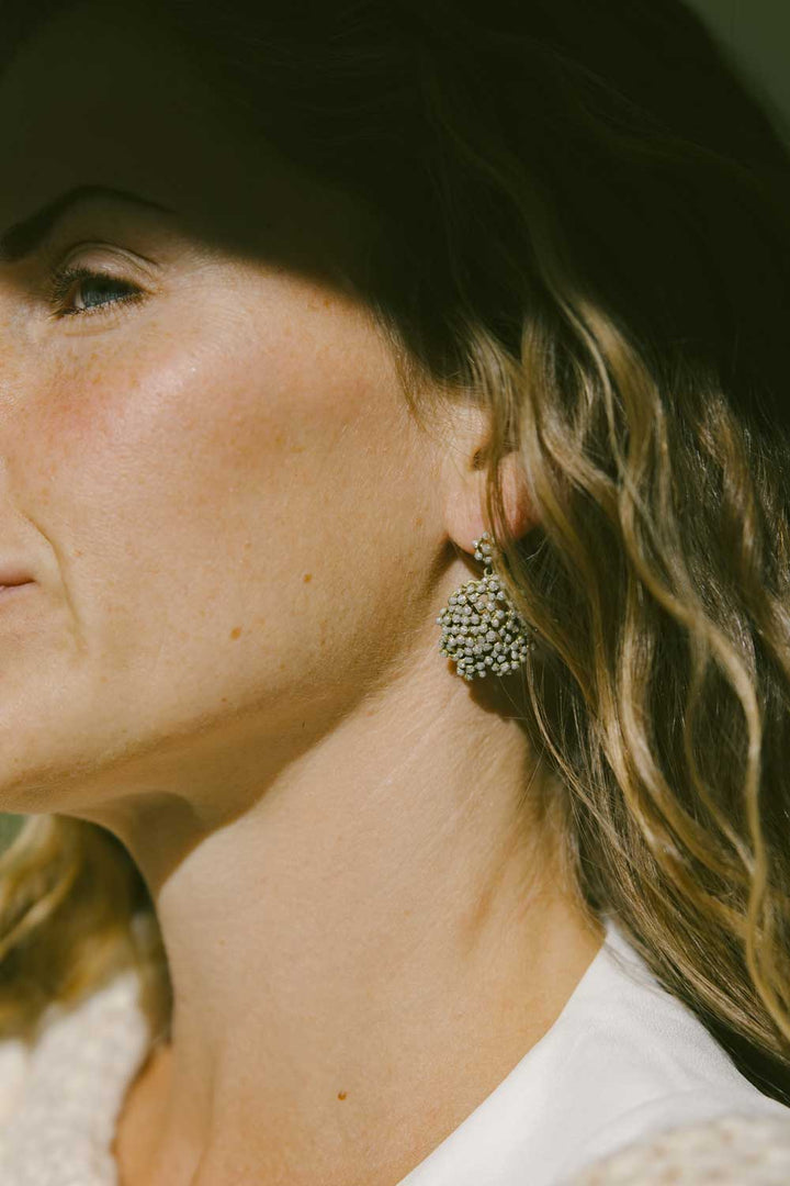 A woman with dark blond wavy hair is wearing a pair of round crystal dust earrings.