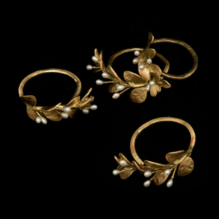 Set of gold napkin rings with leaf and pearl design on a black background
