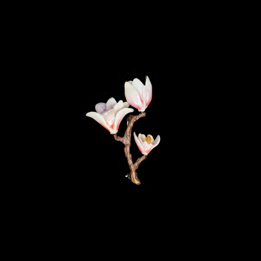 A small brooch with a brown branch with three pale pink and white flowers on a solid black background.