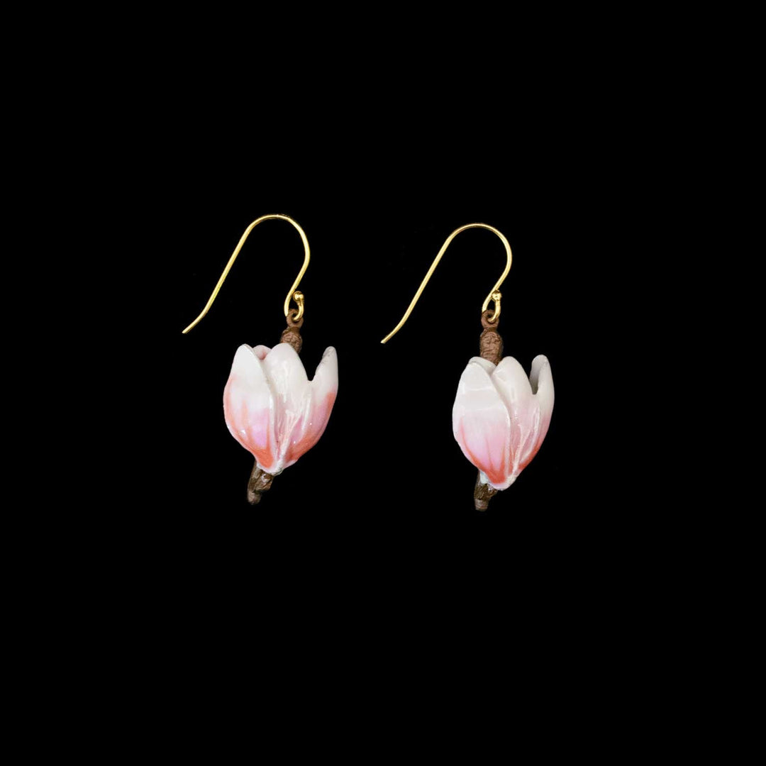 A pair of dangling earrings shaped like small pink and white blossoms on brown branches, suspended from gold fishhook wires, shown against a solid black background.