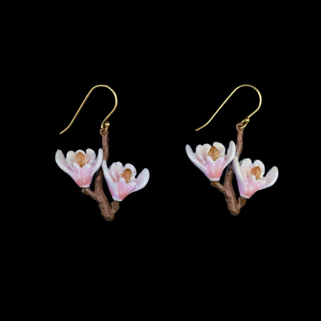 A pair of dangling earrings shaped like small pink and white blossoms on brown branches, suspended from gold fishhook wires, shown against a solid black background.