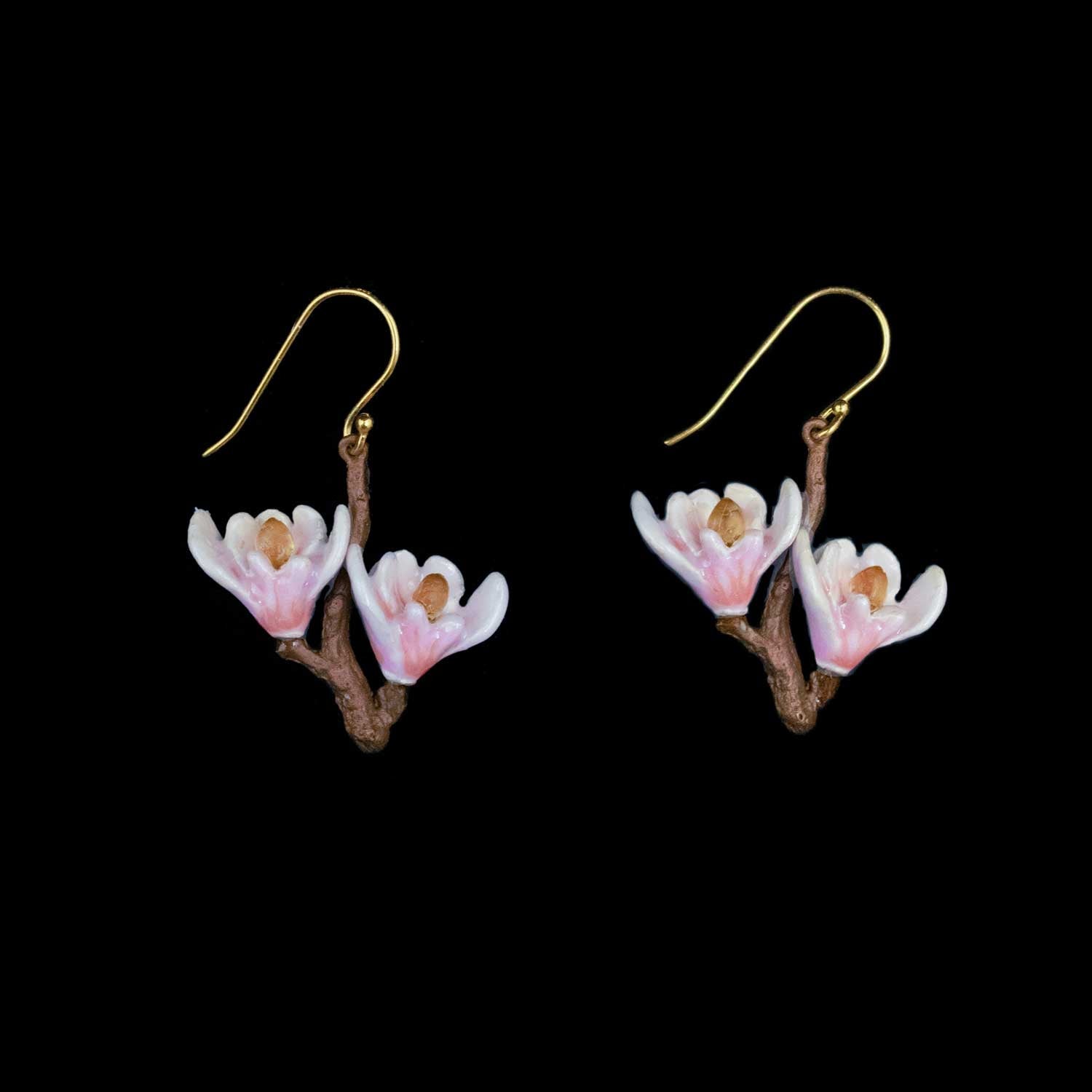 A pair of dangling earrings shaped like small pink and white blossoms on brown branches, suspended from gold fishhook wires, shown against a solid black background.