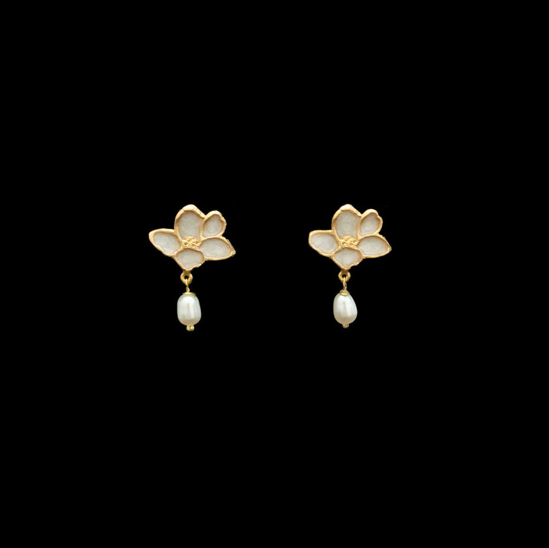 A pair of gold flower-shaped dangle earrings with white enamel petals and a small white pearl drop, shown on a solid black background.
