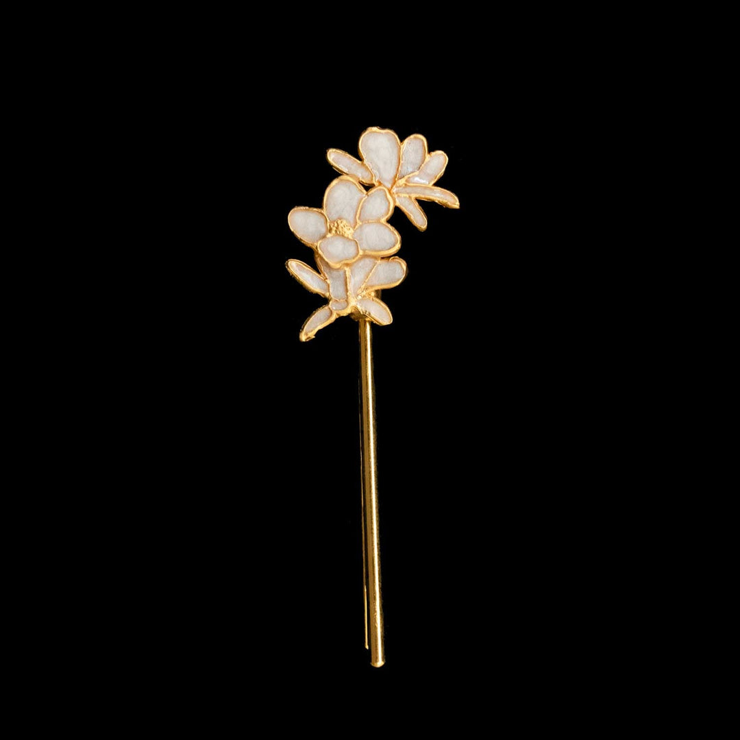 A gold-tone floral hair pin with white enamel petals, shown against a solid black background.