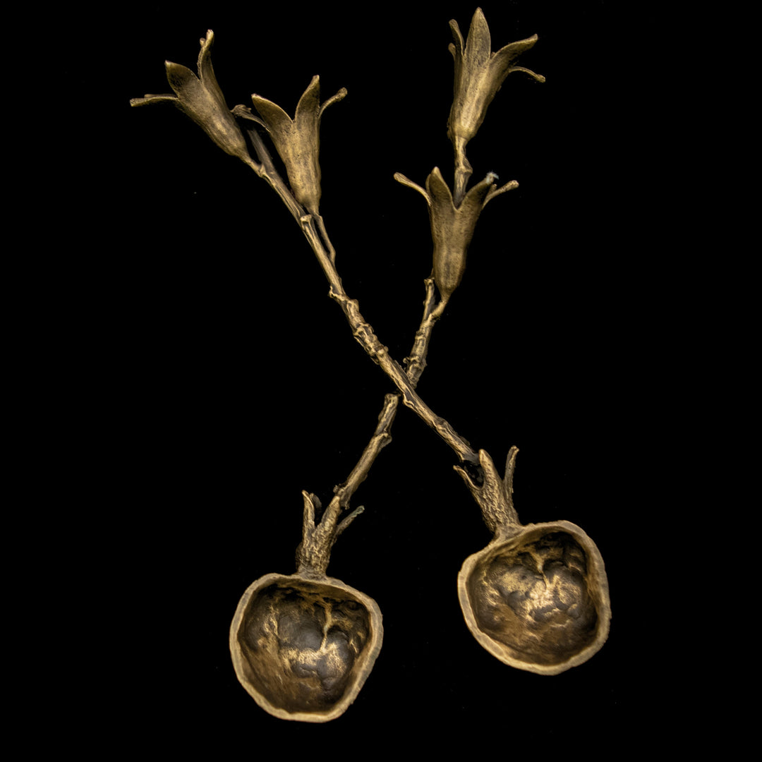 Two dark bronze-colored spoons in the shape of a pomegranate with twigs and flowers on black background