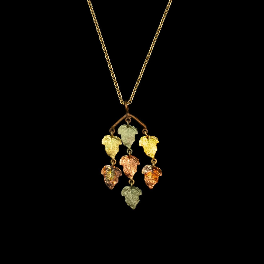 A gold chain necklace with a branch-shaped pendant holding five dangling leaf charms in assorted warm and cool colors, shown against a solid black background.